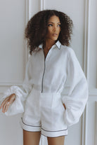 Woman wearing a white outfit with black trim against a neutral background